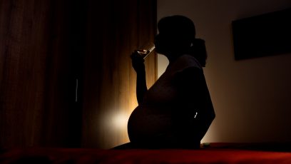 A pregnant woman drinking water in the dark.
