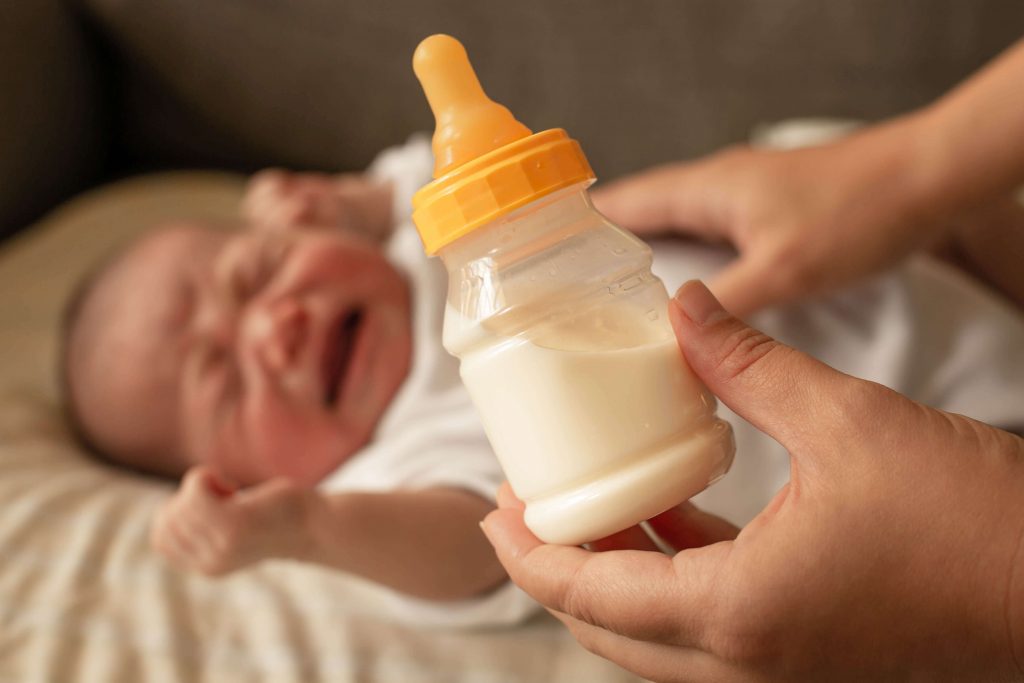 Crying baby with milk in a bottle in front of it.