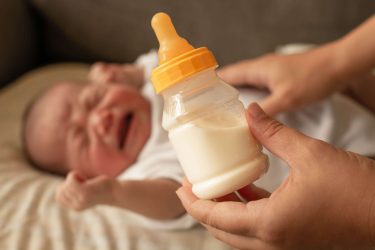 Crying baby with milk in a bottle in front of it.