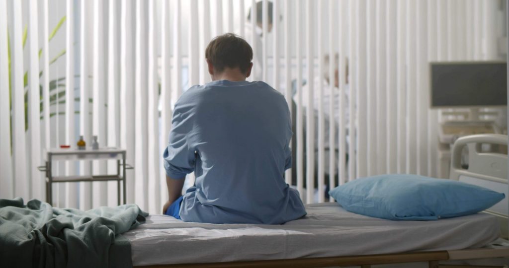 Men in hospital sitting on her bed.